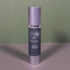 A silver and dark gray bottle of Divina Timeless Moisture stands upright on a gray surface against a green background, displaying white text and a minimalist plant logo.