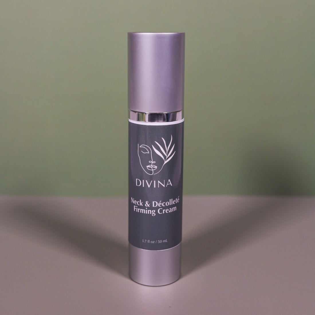 A bottle of Divina Neck &amp; Décolleté Firming Cream with a gray label and silver cap rests on a flat surface against a muted green background. This luxurious cream is designed to firm the neck area and reduce wrinkles.