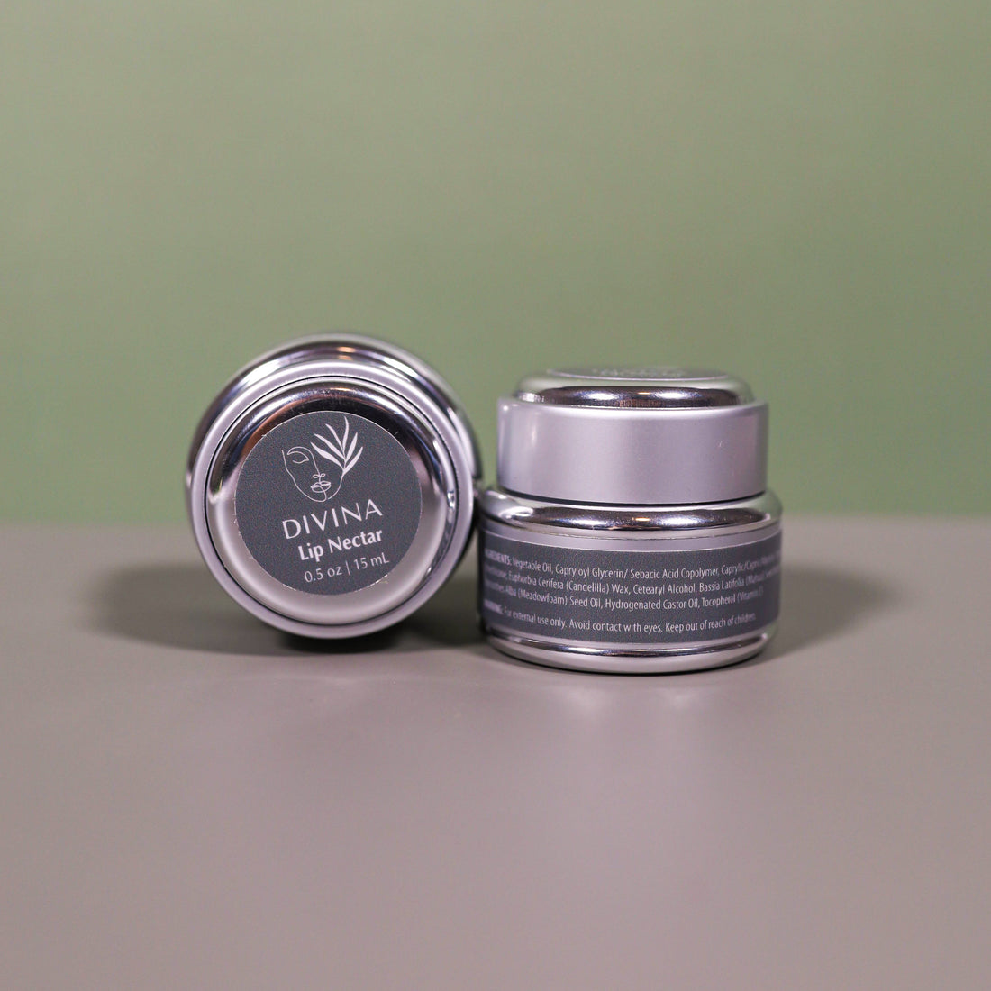 Two small silver jars of Divina’s Lip Nectar, a luxurious lip treatment, sit against a neutral background—one upright displaying the side label, the other tilted to spotlight the lid and Divina branding.